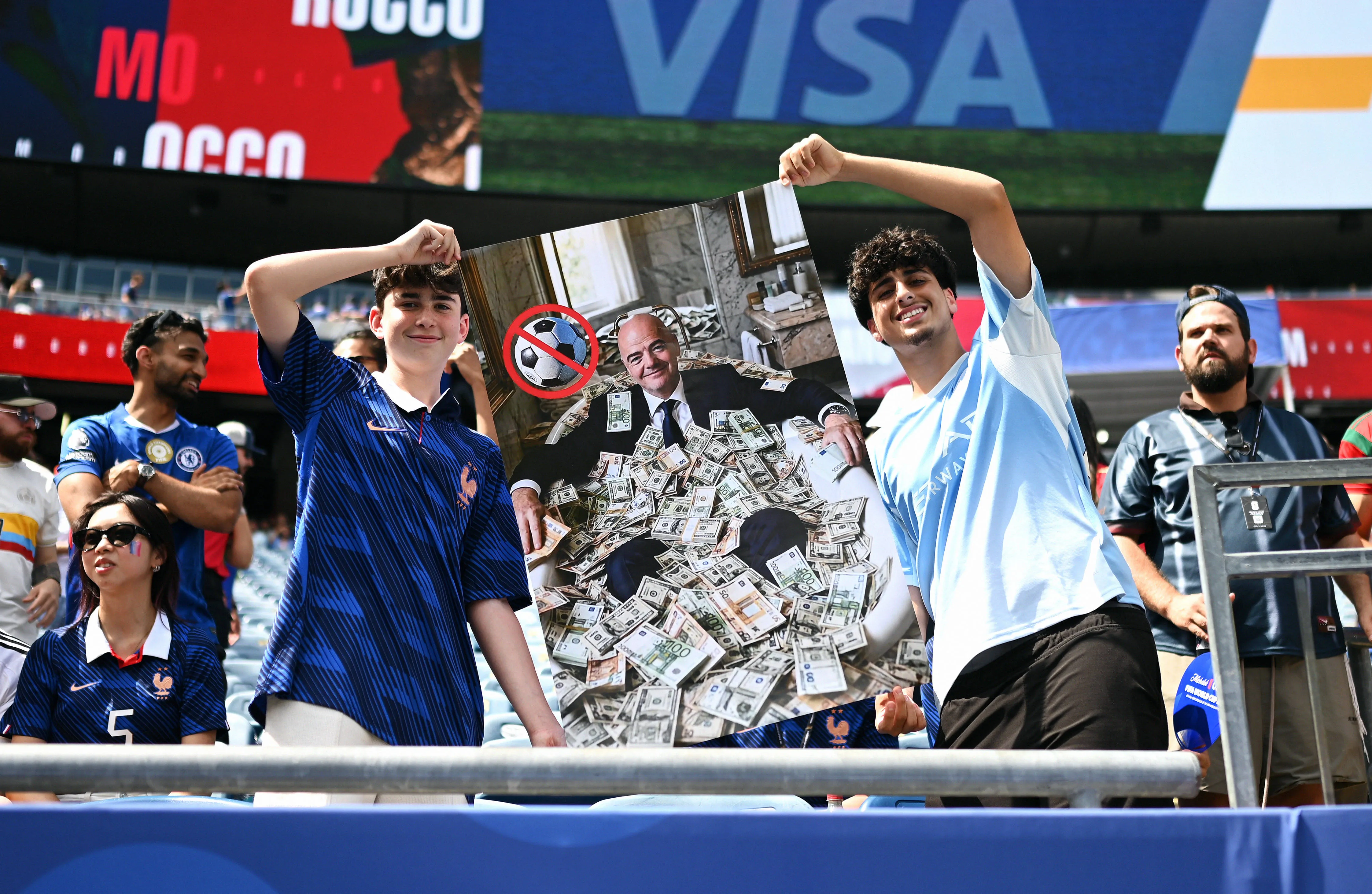 Two young French fans hold up a sign showing FIFA President Gianni Infantino in a bathtub full of money