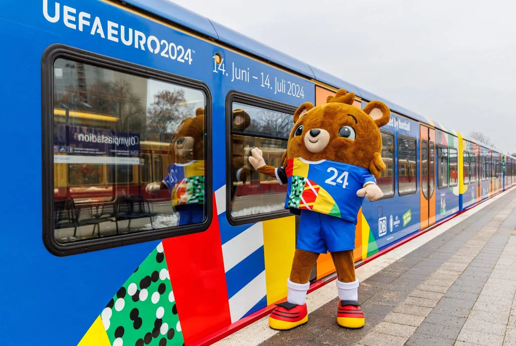 A class 481 S-Bahn train in the European Championship design stops at the Olympiastadion S-Bahn station. The official European Championship mascot stands in front of a train with the lettering: "UEFA Euro 2024" | Euro 2024 host stadiums | Euro 2024 stadiums | Euro 2024 stadiums map